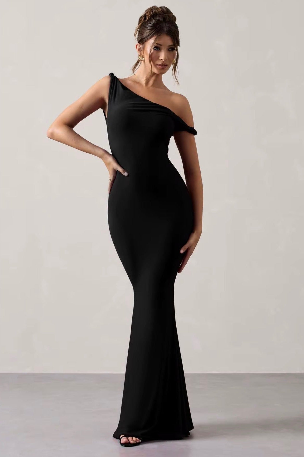 Woman wearing a black one-shoulder dress against a plain background
